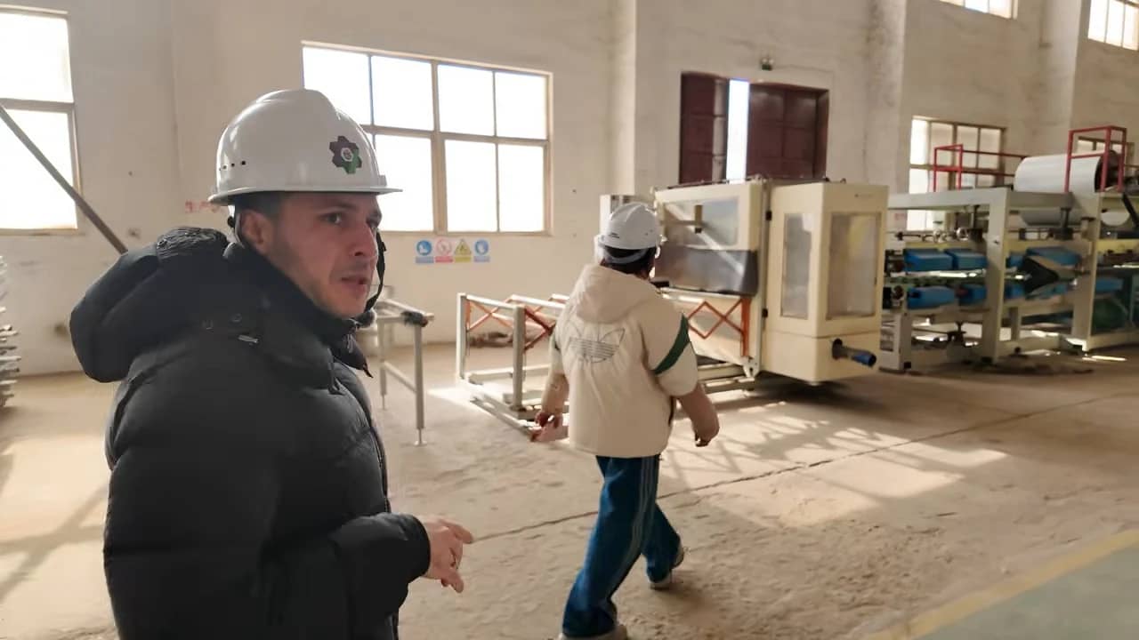 Deux personnes portant un casque visitent un atelier devant une ligne de machines.