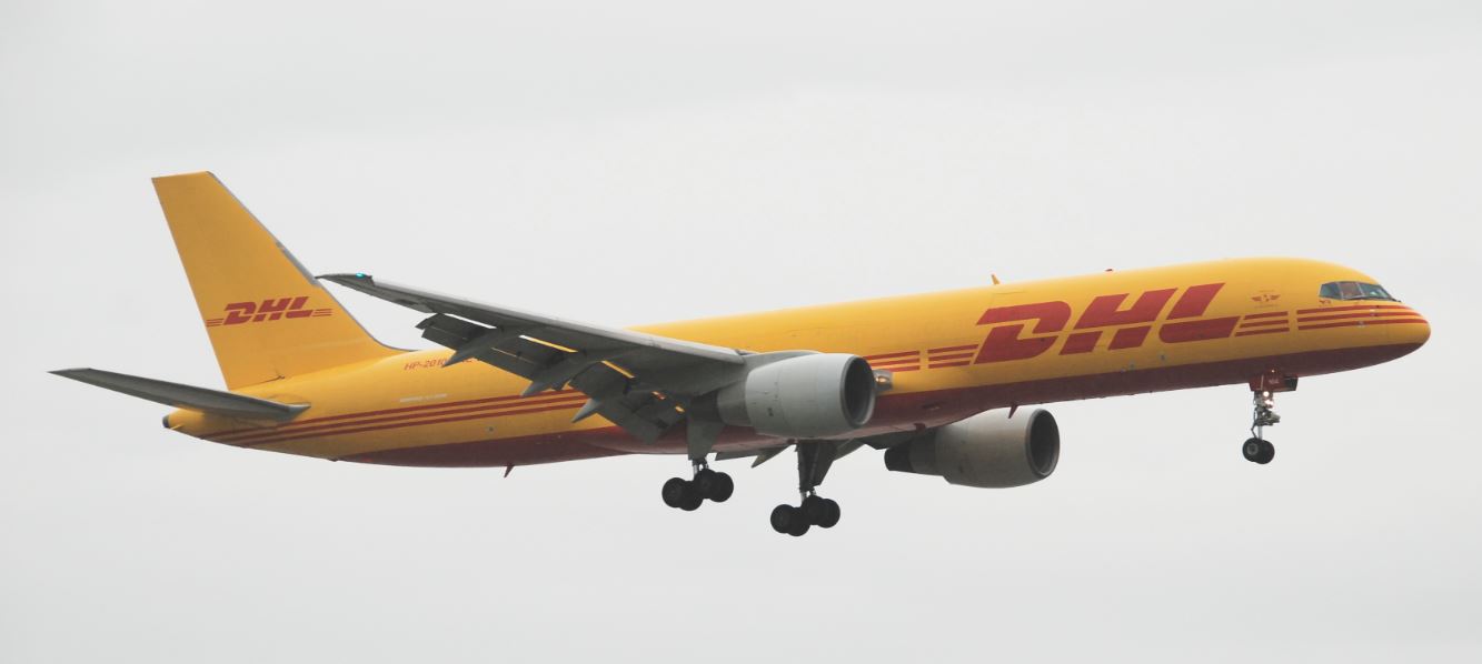 Une compagnie de fret aérien DHL, avec un avion cargo approchant pour l'atterrissage, se profile contre un ciel nuageux.